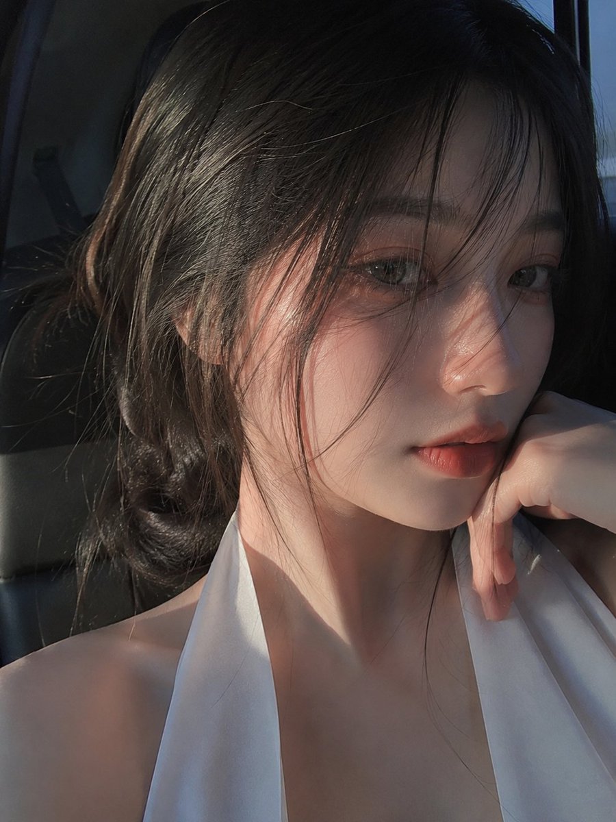 A tight, half-face portrait of a young woman with damp wisps of dark hair across one eye. Warm sunset gold and cool blue shadows meet on her skin, and the…